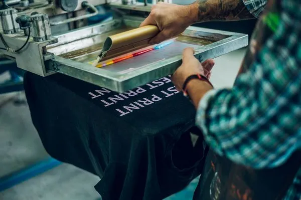 male wearing green shirt doing screen printing process in cheez clothing factory
